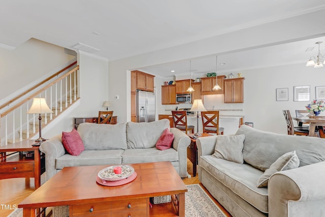 living room with visible vents, light wood-style flooring, stairway, ornamental molding, and an inviting chandelier