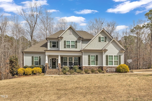 craftsman-style house featuring stone siding, a shingled roof, a front lawn, and covered porch