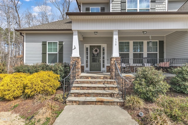 entrance to property featuring a shingled roof and covered porch