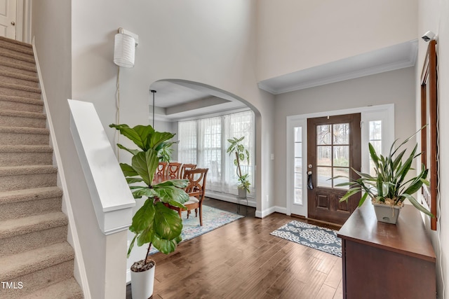 entryway with dark wood-style floors, ornamental molding, stairway, and arched walkways