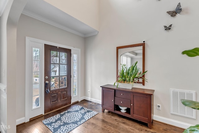 foyer entrance featuring dark wood-style floors, arched walkways, visible vents, and baseboards