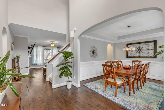 dining area with arched walkways, dark wood-type flooring, ornamental molding, wainscoting, and stairs