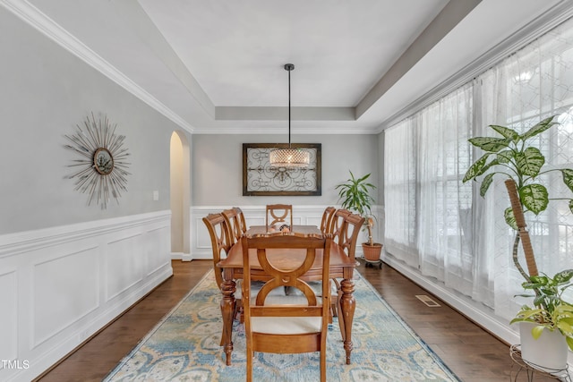 dining room with arched walkways, a wainscoted wall, visible vents, dark wood finished floors, and a raised ceiling