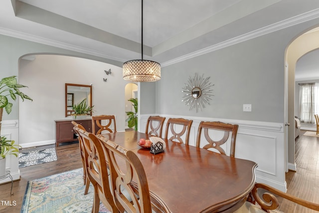 dining space with arched walkways, crown molding, a tray ceiling, and wood finished floors