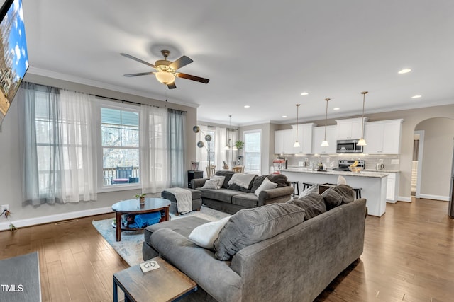 living area featuring arched walkways, dark wood-style flooring, baseboards, and crown molding