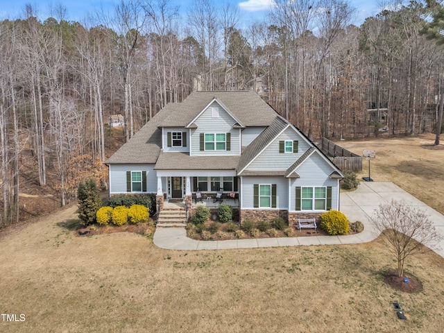 view of front of home with driveway, stone siding, roof with shingles, and a front yard