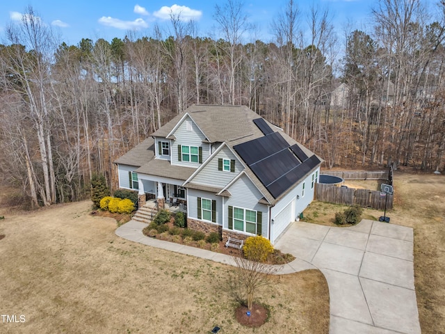 craftsman house with driveway, solar panels, stone siding, fence, and a front lawn