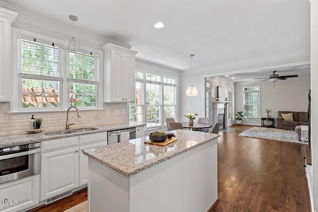 kitchen with stainless steel appliances, ornamental molding, white cabinets, a sink, and a kitchen island