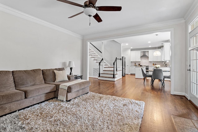 living area featuring stairs, ceiling fan, ornamental molding, and wood finished floors