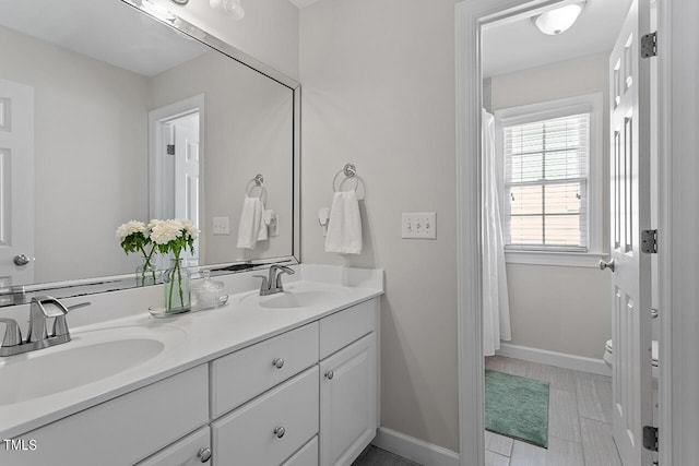 full bathroom featuring toilet, a sink, baseboards, and double vanity