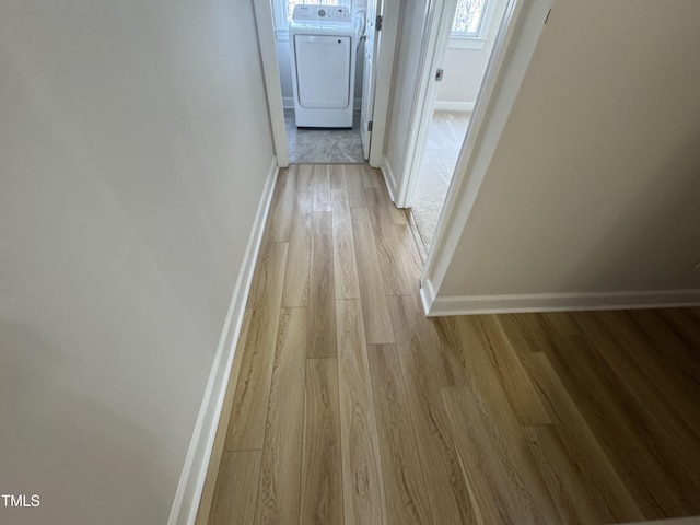 corridor with light wood finished floors, baseboards, and washer and dryer