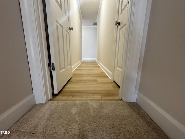 hallway featuring baseboards, light wood-type flooring, visible vents, and light colored carpet