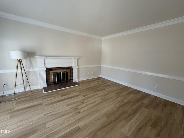 unfurnished living room featuring a brick fireplace, baseboards, ornamental molding, and wood finished floors