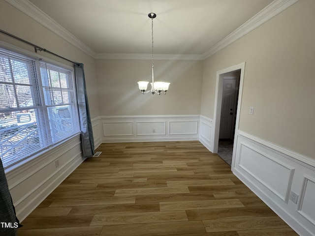 unfurnished dining area featuring a wainscoted wall, ornamental molding, a notable chandelier, and wood finished floors