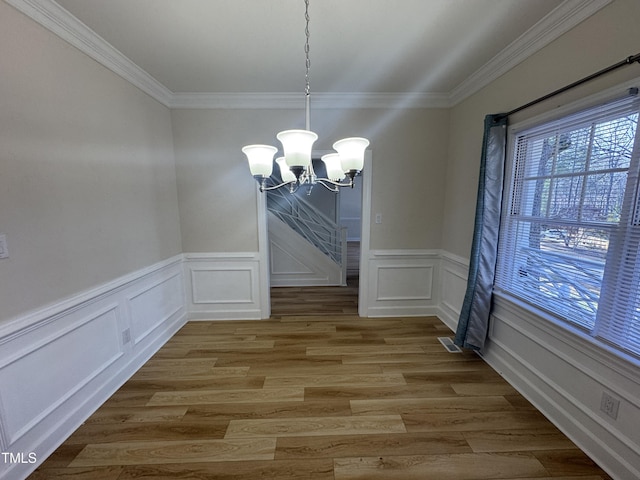 unfurnished dining area featuring visible vents, crown molding, a chandelier, and wood finished floors