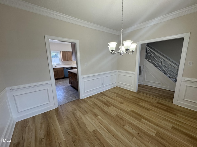 unfurnished dining area featuring light wood finished floors, a chandelier, a wainscoted wall, and ornamental molding