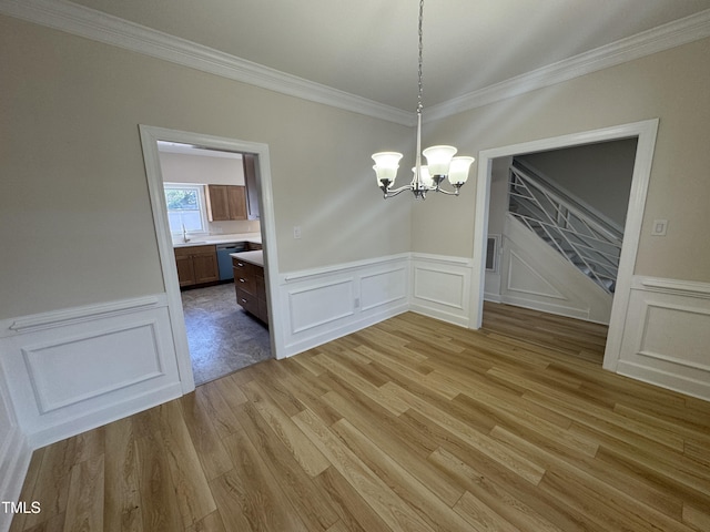 unfurnished dining area with light wood-style floors, crown molding, a sink, and an inviting chandelier