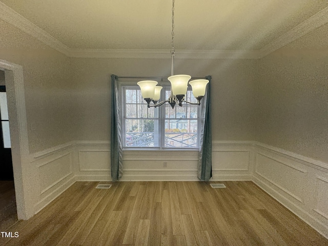 unfurnished dining area with an inviting chandelier, visible vents, wood finished floors, and a wainscoted wall