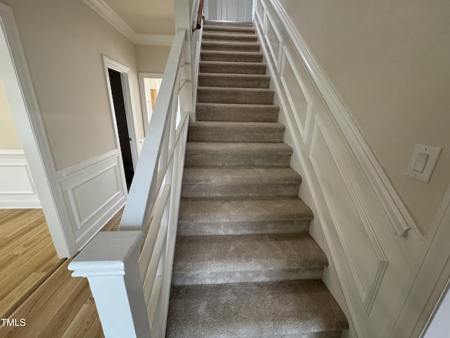 stairway featuring wainscoting, a decorative wall, crown molding, and wood finished floors