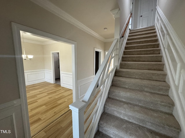 stairs featuring ornamental molding, a chandelier, a wainscoted wall, and wood finished floors