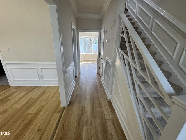 hall with light wood-type flooring, a wainscoted wall, crown molding, and stairway