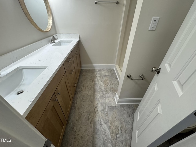 full bath with double vanity, a sink, and baseboards