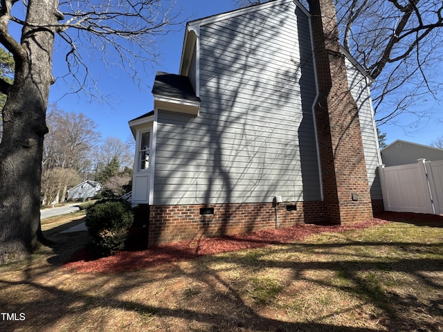 view of side of home featuring a yard, crawl space, fence, and a chimney