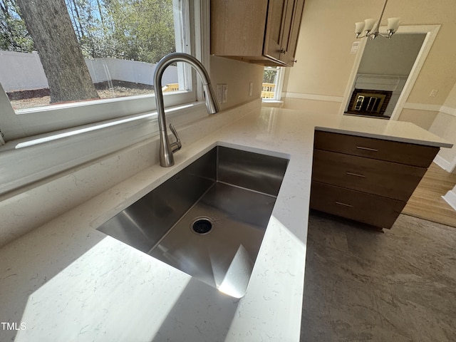 interior details featuring a glass covered fireplace, a peninsula, an inviting chandelier, light stone countertops, and a sink