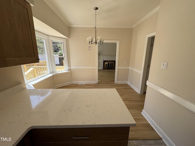 interior space with a notable chandelier, a glass covered fireplace, wood finished floors, and crown molding