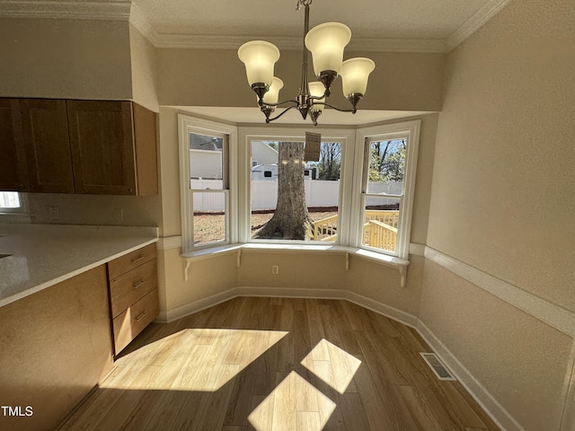 unfurnished dining area with baseboards, visible vents, dark wood-style flooring, crown molding, and a notable chandelier