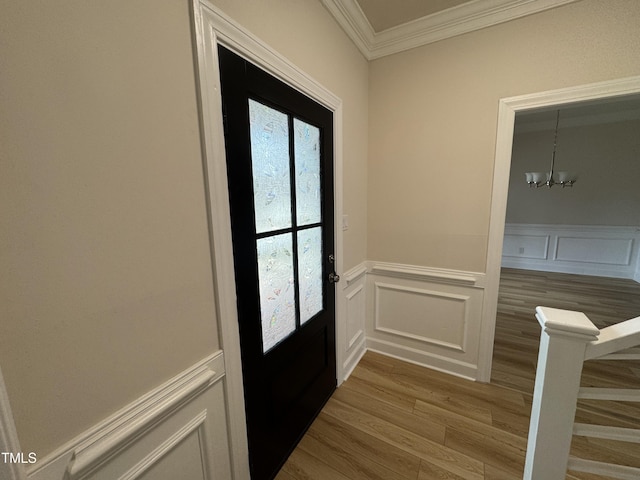 entryway with a decorative wall, an inviting chandelier, ornamental molding, wainscoting, and wood finished floors