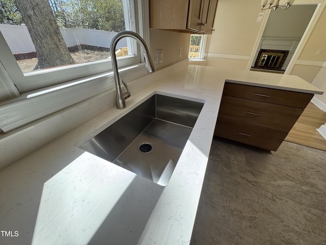 details featuring a peninsula, light stone countertops, a sink, and a glass covered fireplace