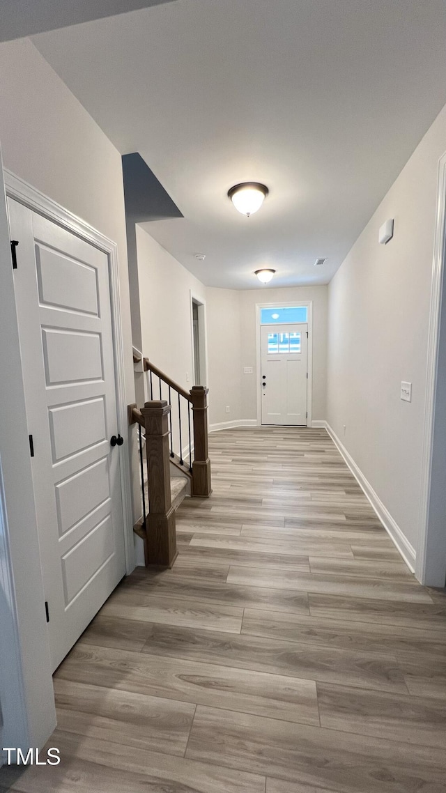 hallway featuring light wood finished floors, stairway, visible vents, and baseboards