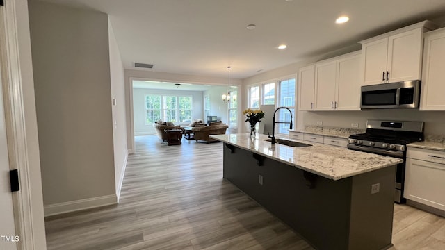 kitchen with pendant lighting, stainless steel appliances, a kitchen island with sink, a sink, and white cabinetry