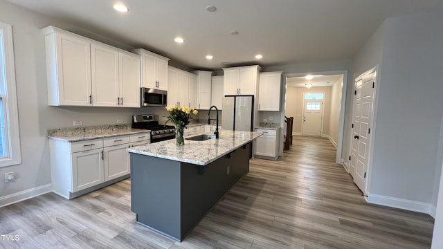 kitchen featuring white cabinets, light stone countertops, stainless steel appliances, and a sink