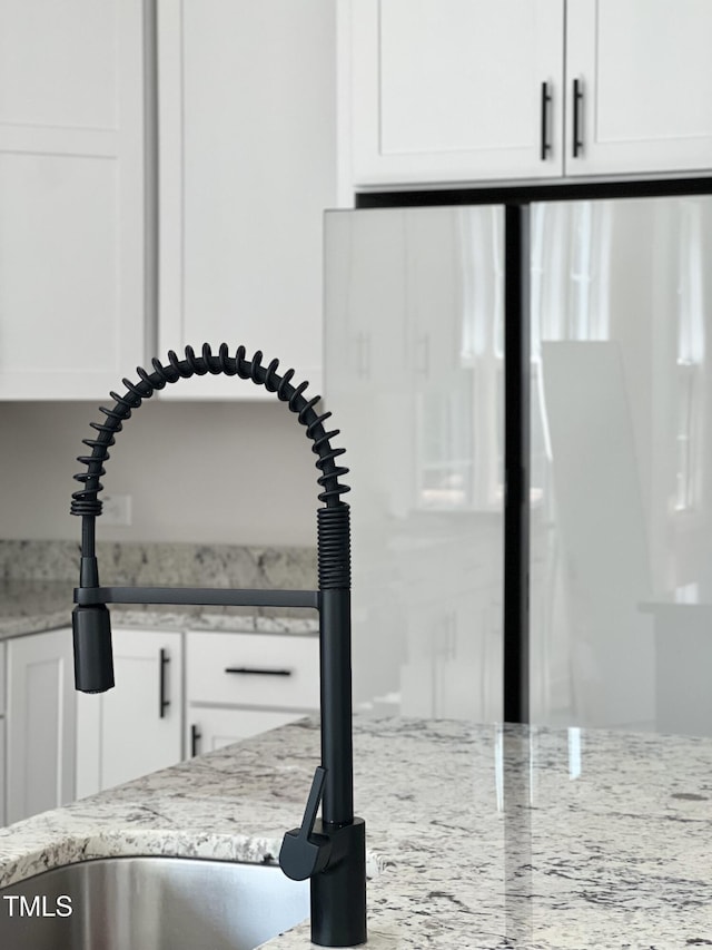 interior details with light stone counters, refrigerator, white cabinetry, and a sink