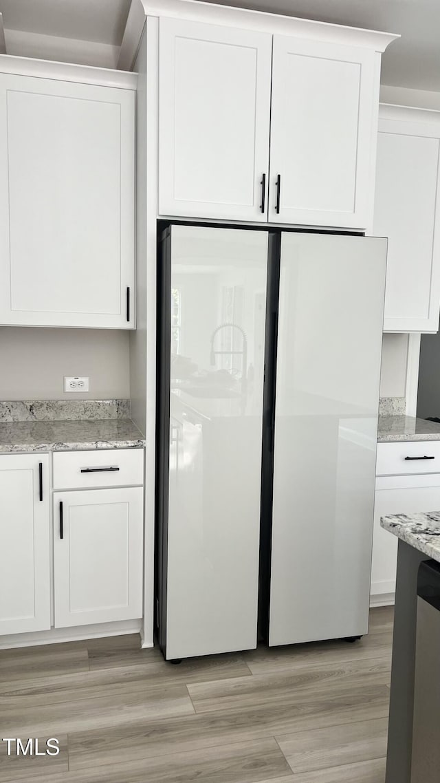 interior space with light wood-type flooring, light stone countertops, freestanding refrigerator, and white cabinets