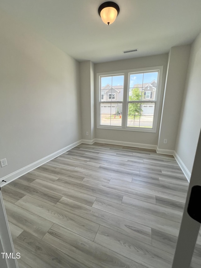 empty room with light wood-type flooring, visible vents, and baseboards