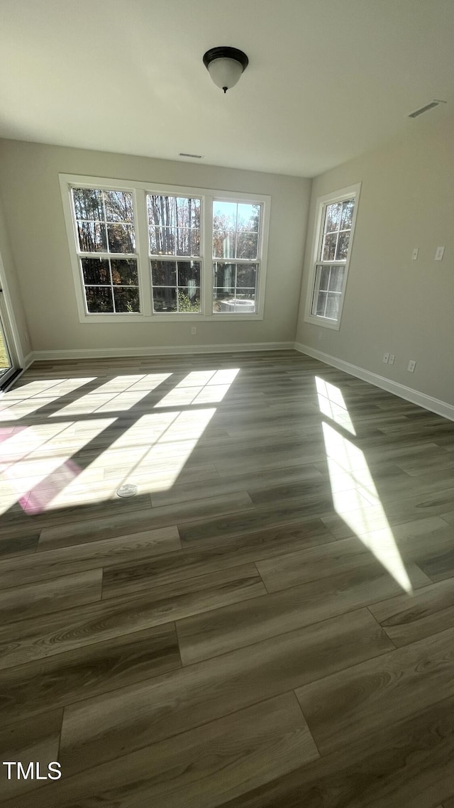 spare room with wood finished floors, visible vents, and baseboards