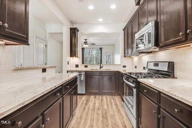 kitchen featuring backsplash, light wood-style flooring, appliances with stainless steel finishes, a sink, and light stone countertops