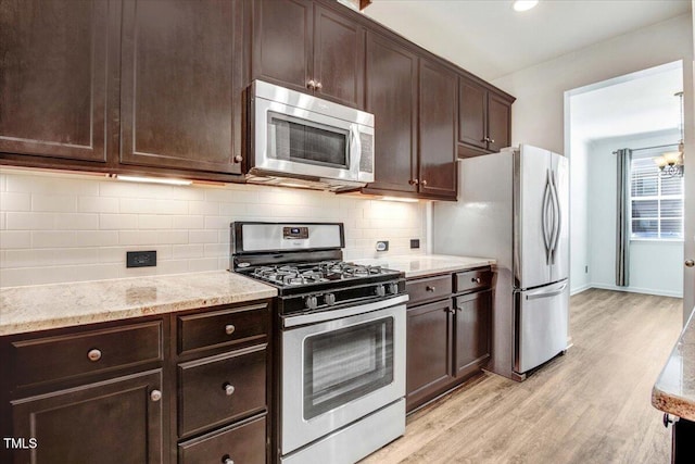 kitchen with light wood finished floors, decorative backsplash, light stone counters, appliances with stainless steel finishes, and dark brown cabinets