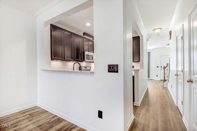 corridor featuring baseboards, light wood finished floors, a sink, and crown molding