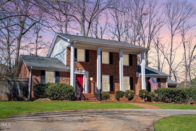 greek revival house featuring a shingled roof, fence, a front lawn, and brick siding