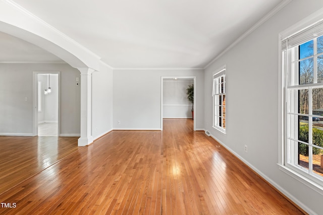 spare room with arched walkways, light wood-style flooring, baseboards, ornate columns, and crown molding