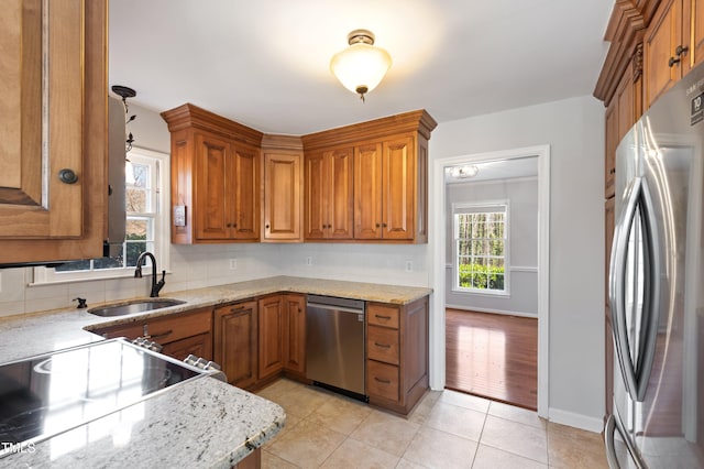 kitchen with appliances with stainless steel finishes, brown cabinetry, a sink, and light stone counters