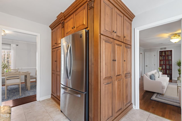 kitchen with baseboards, light tile patterned flooring, brown cabinets, and freestanding refrigerator