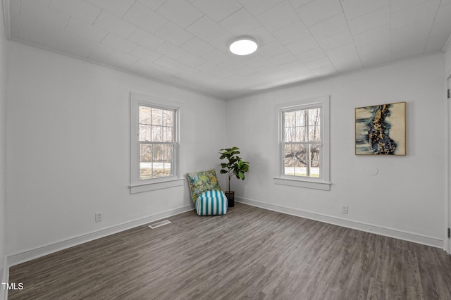 unfurnished room with baseboards, dark wood-style floors, a wealth of natural light, and visible vents