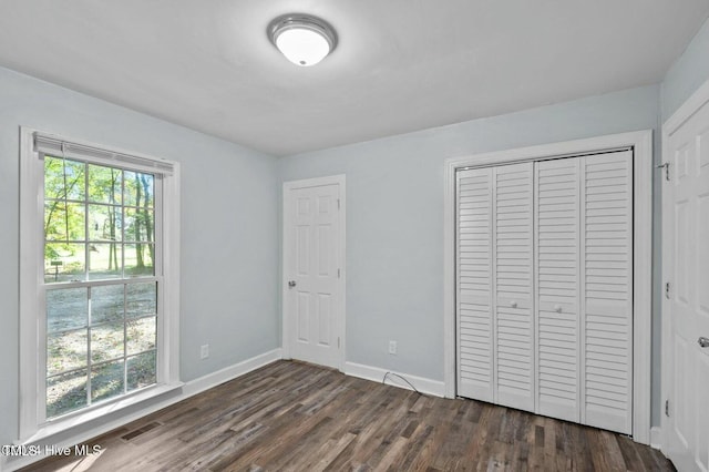 unfurnished bedroom with dark wood-style floors, a closet, visible vents, and baseboards