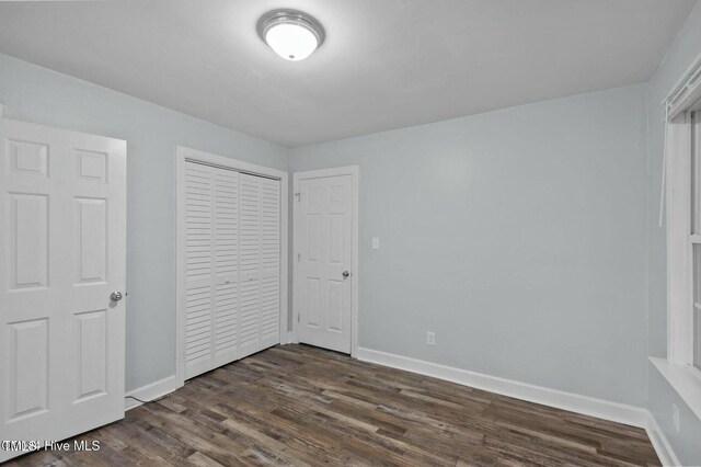 unfurnished bedroom with a closet, dark wood finished floors, and baseboards