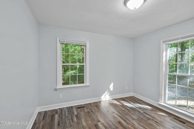 empty room with dark wood-type flooring, visible vents, and baseboards